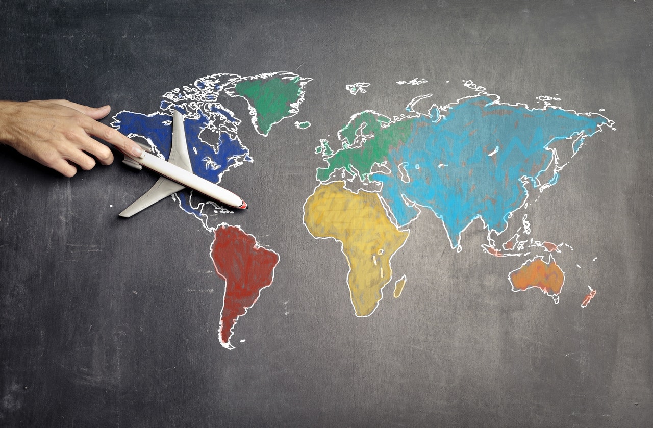 miniature airplane traveling across a flat rendition of the world map on a blackboard