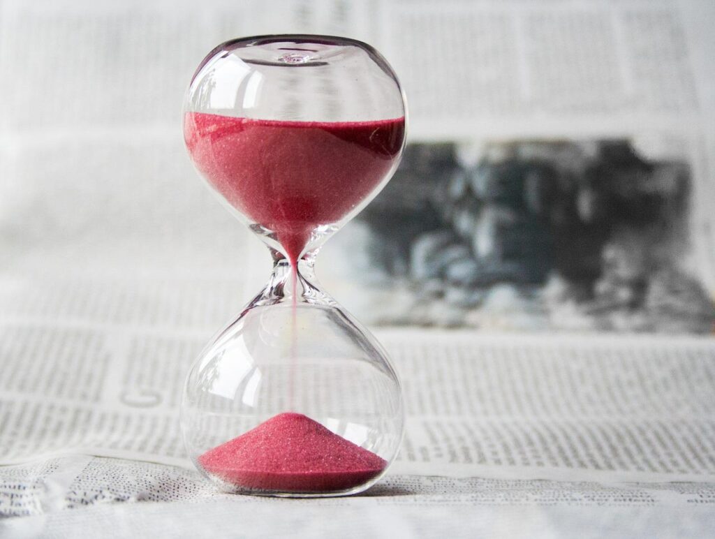 An hourglass with red velvet sand standing on an open newspaper