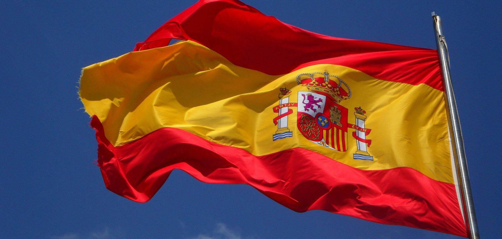 Spanish flag on mast against a blue sky backdrop